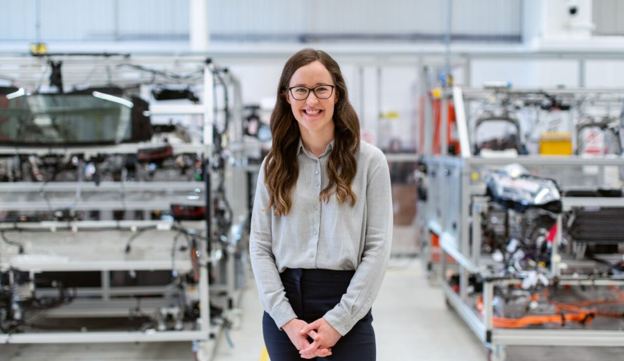 Une ingénieure souriante pose dans un atelier industriel, entre deux bancs d'assemblage