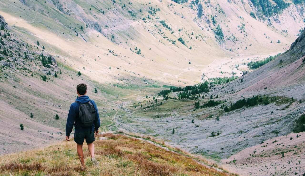 Un randonneur avec un sac à dos contemple une large vallée de montagne, de dos