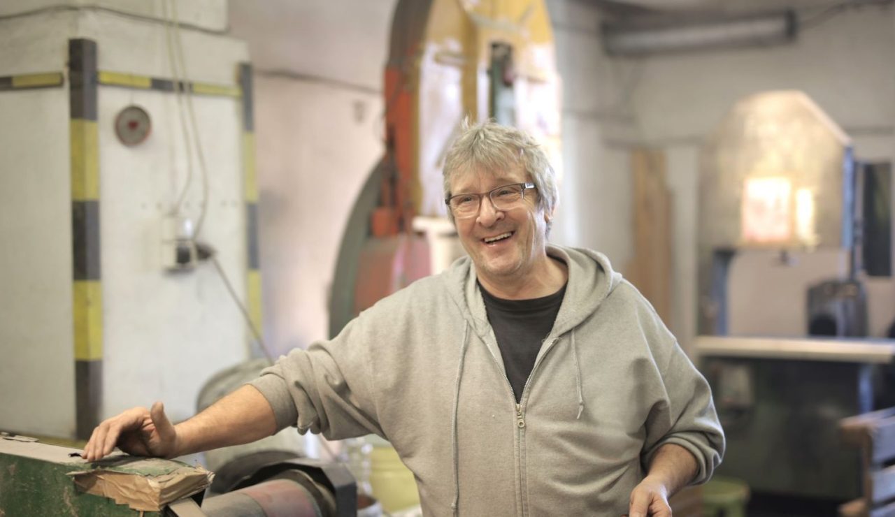 Artisan aux cheveux blancs souriant dans un atelier lumineux, en fin de carrière professionnelle