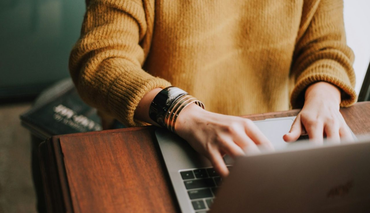 Une personne en pull moutarde tape sur son ordinateur portable, symbole de la recherche d'emploi en 2026