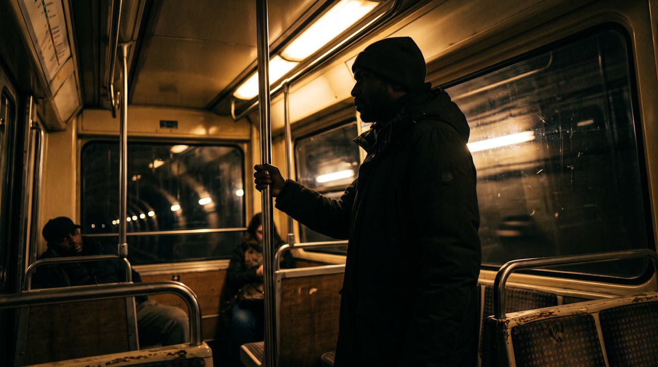 Une personne debout a contre-jour dans une rame de metro en mouvement, le soir