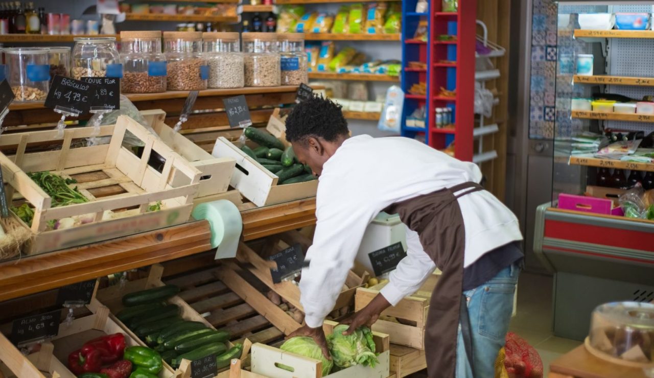 Employé de commerce en tablier disposant des cageots de légumes frais dans un magasin lumineux