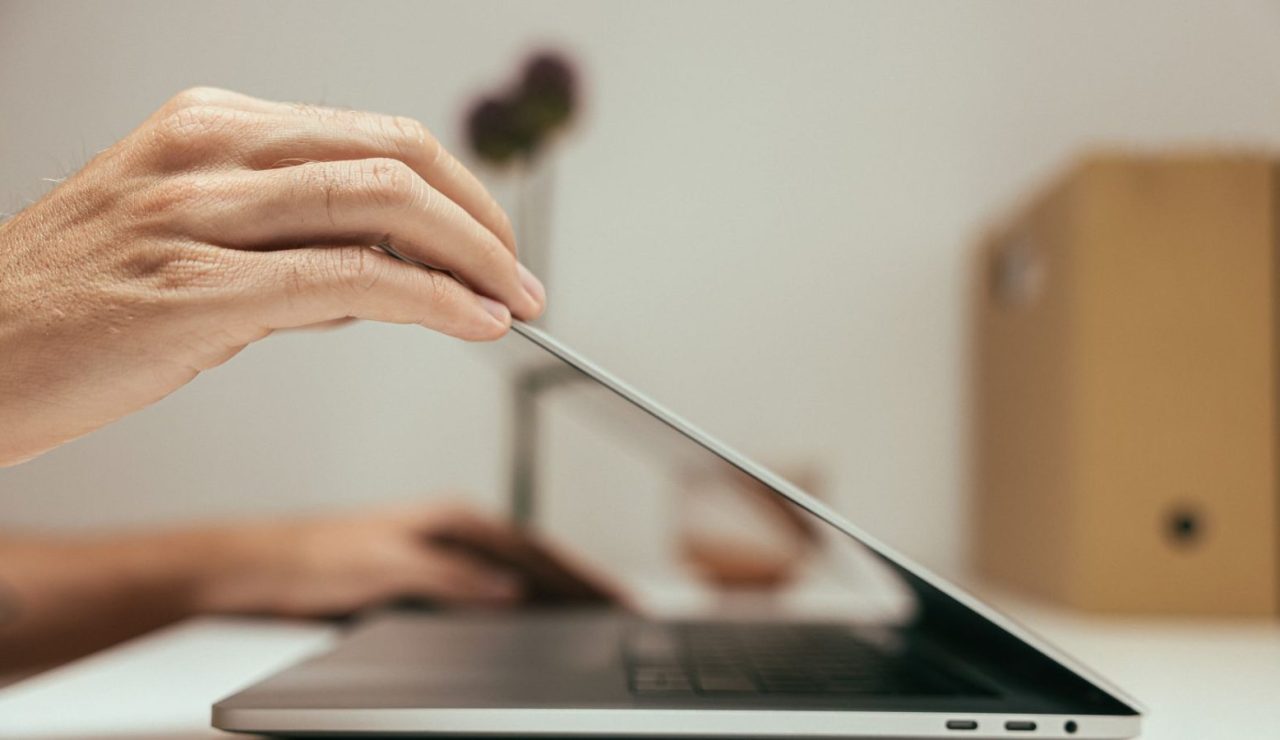 Main refermant un ordinateur portable sur un bureau clair et épuré en fin de journée de travail