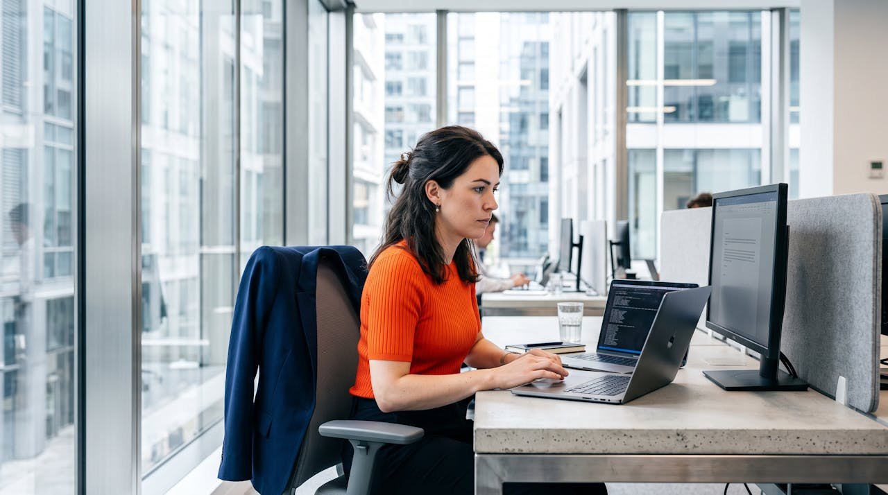 Une candidate travaille sur son ordinateur portable dans un espace de coworking vitré, en train d'utiliser un outil d'intelligence artificielle pour sa recherche d'emploi