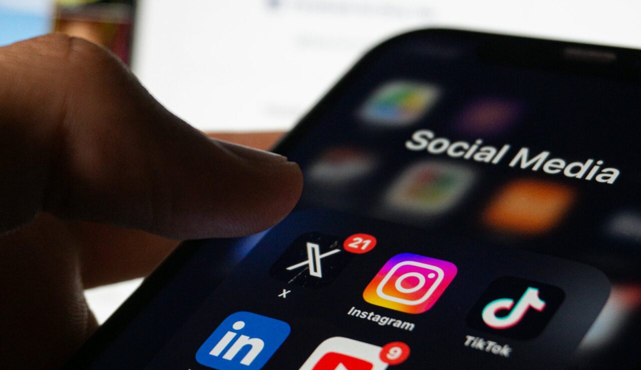 Un pouce ouvre le dossier réseaux sociaux d’un smartphone, avec les applications LinkedIn, Instagram et TikTok