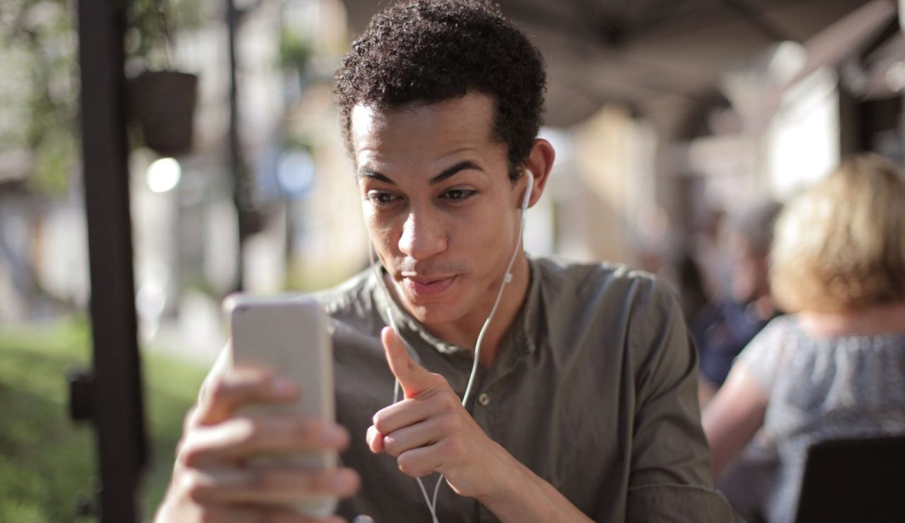 Homme souriant consultant son téléphone à la terrasse d'un café en ville