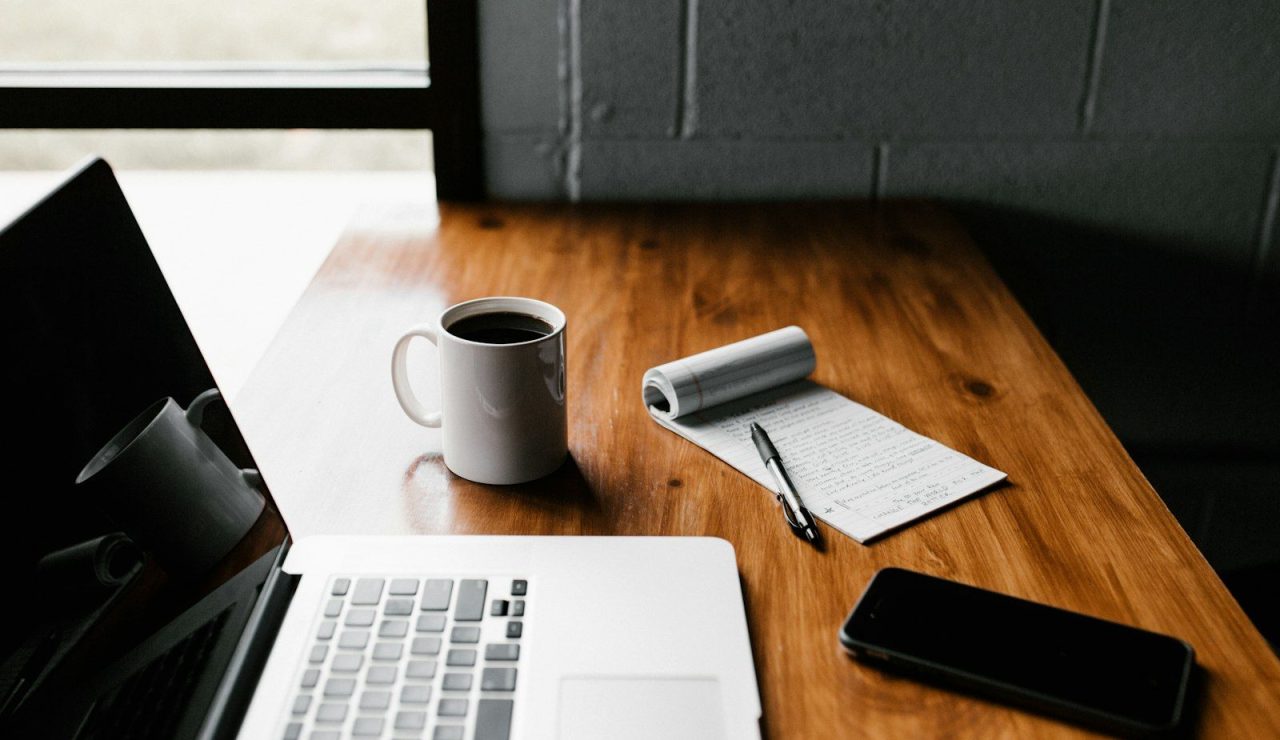Un candidat prend le temps de réfléchir à son avenir professionnel devant son ordinateur, avec un carnet de notes et un café