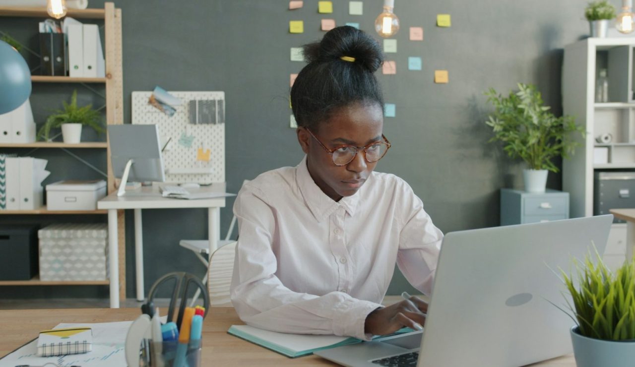 Jeune diplômée assise à un bureau lumineux, concentrée sur son ordinateur portable pendant sa recherche de premier emploi