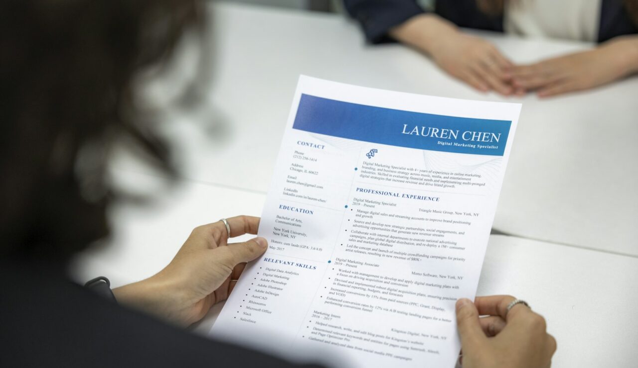 Une recruteuse lit attentivement le CV imprimé d’une candidate lors d’un entretien d’embauche