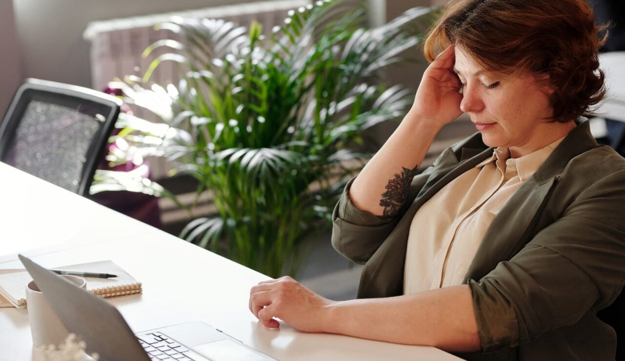 Salariée épuisée, la main sur le front, devant son ordinateur portable dans un bureau lumineux