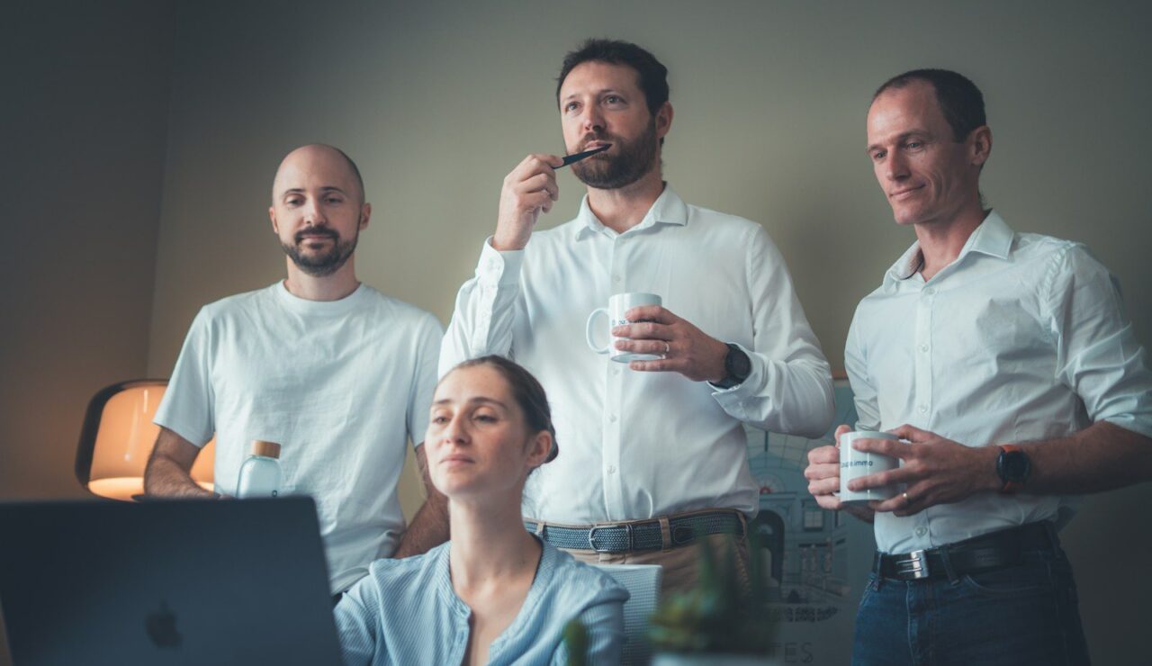 Trois collègues, tasse de café à la main, regardent l'écran d'une collègue qui étudie une candidature