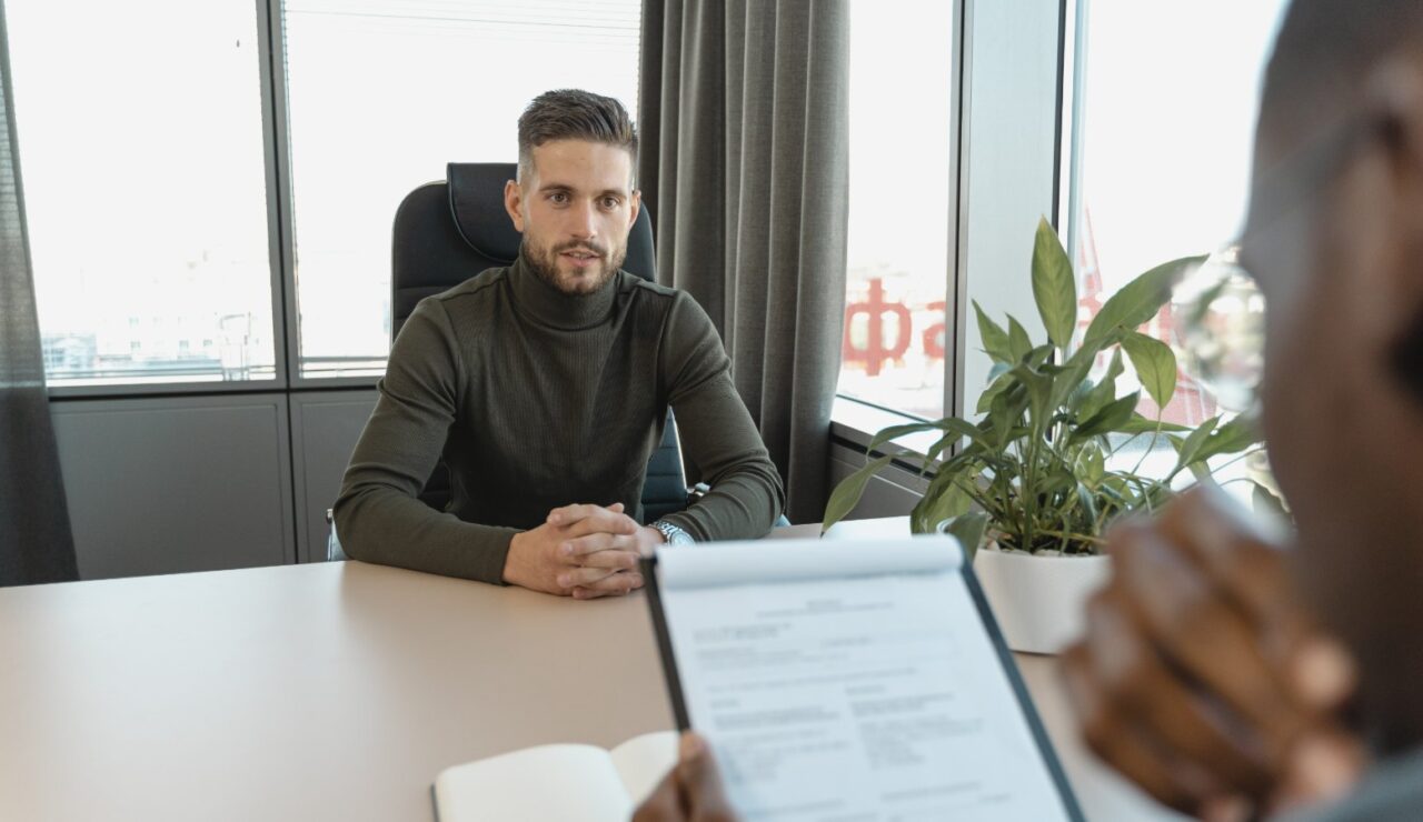 Un candidat assis face a un recruteur qui tient son CV lors d un entretien d embauche dans un bureau lumineux