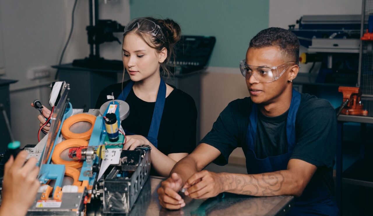 Deux jeunes en tablier bleu travaillent sur un montage electronique dans un atelier lumineux
