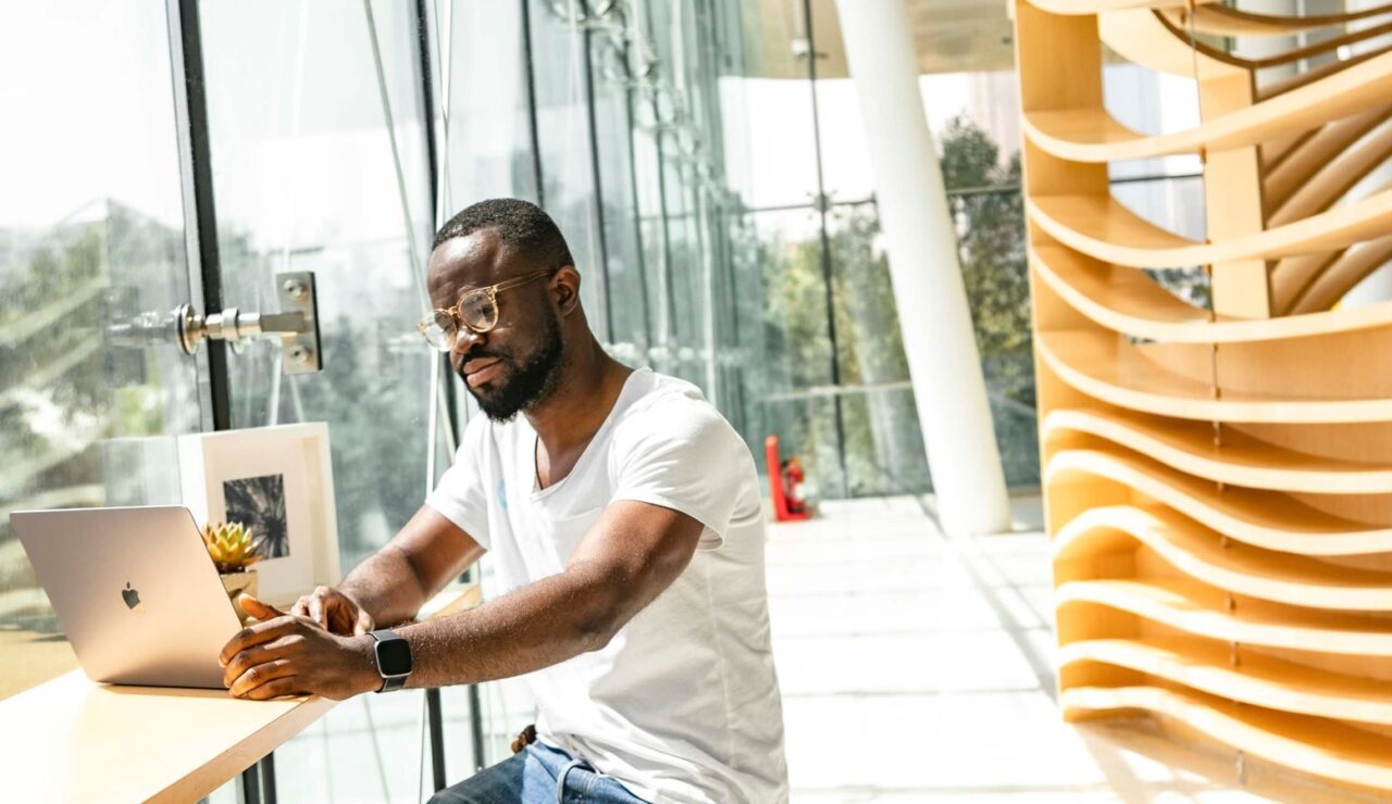 Candidat consultant des offres d'emploi sur son ordinateur portable dans un batiment vitre contemporain