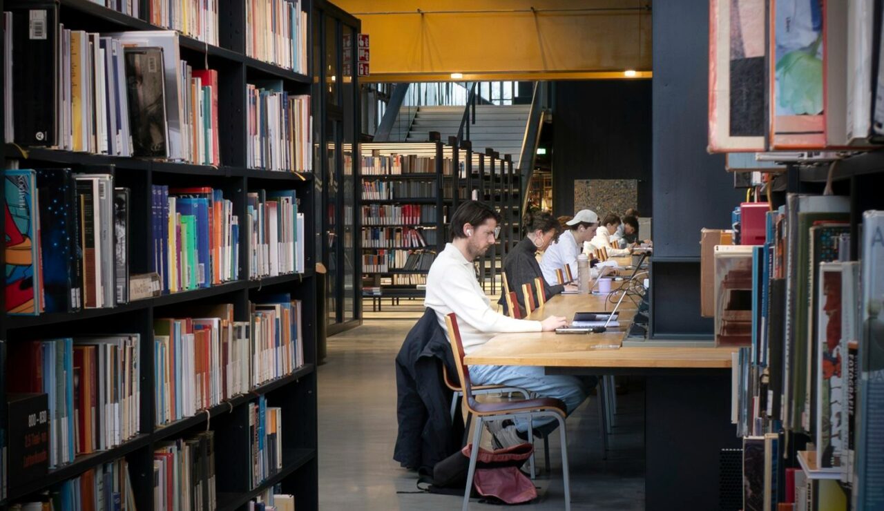 Des candidats rédigent leur candidature sur ordinateur portable à une longue table de bibliothèque moderne