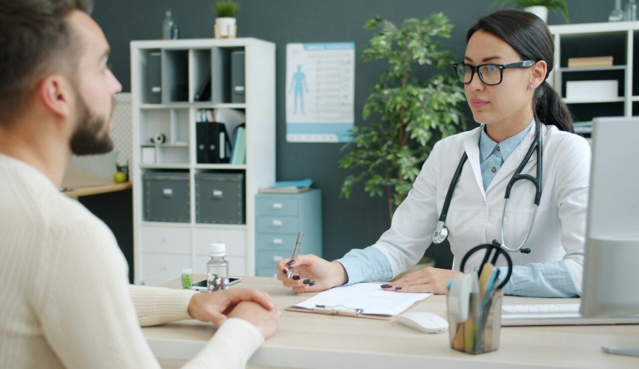 Un salarié échange avec une médecin dans un cabinet médical clair, un dossier posé sur le bureau