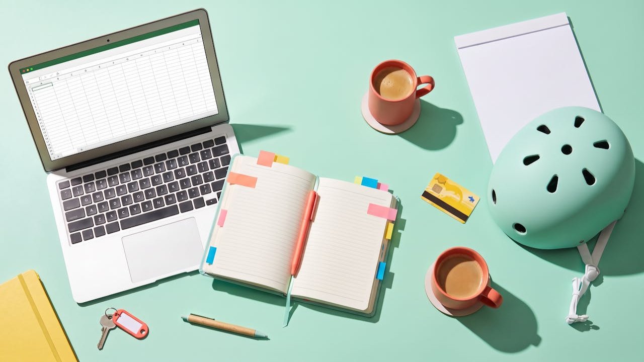 Bureau d'étudiant vu du dessus avec ordinateur portable, agenda à onglets, casque de vélo et cafés, préparation d'une recherche d'alternance