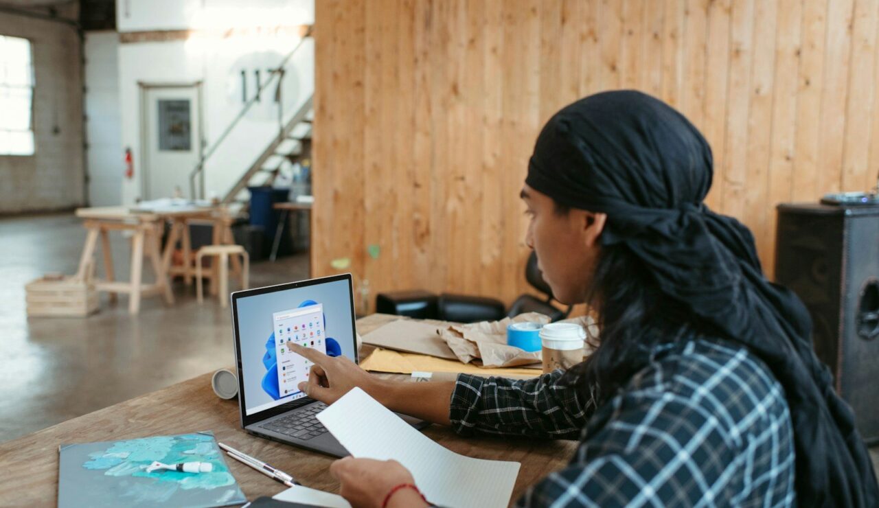 Jeune homme portant un bandana noir qui consulte un ordinateur portable dans un atelier partagé aux murs de bois